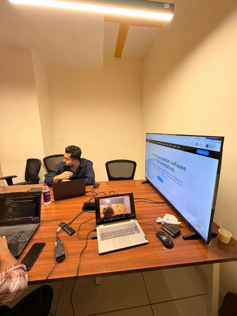 The Avlys workspace with laptops, a shared display, and a team member at the table.